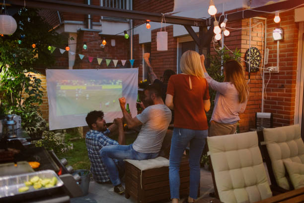 Friends watching sports on big screen in backyard. Drinking beer and cheering.